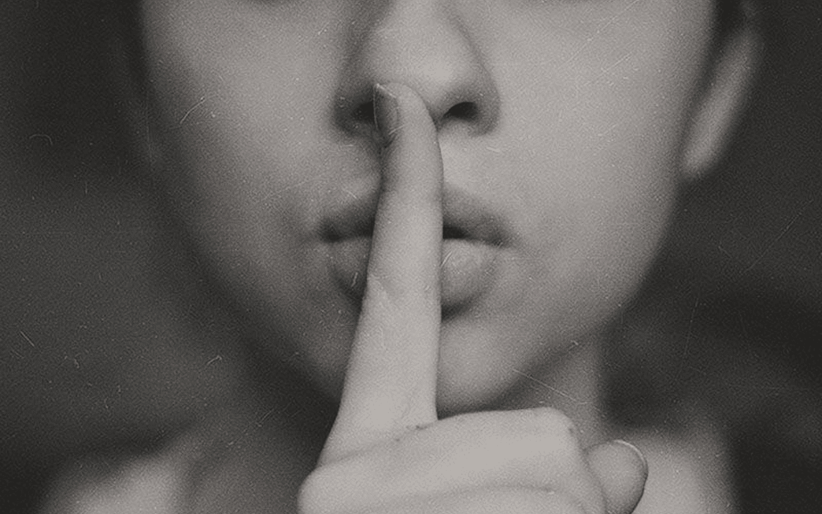 Black and white photo of a woman holding fingers to lips to show shush