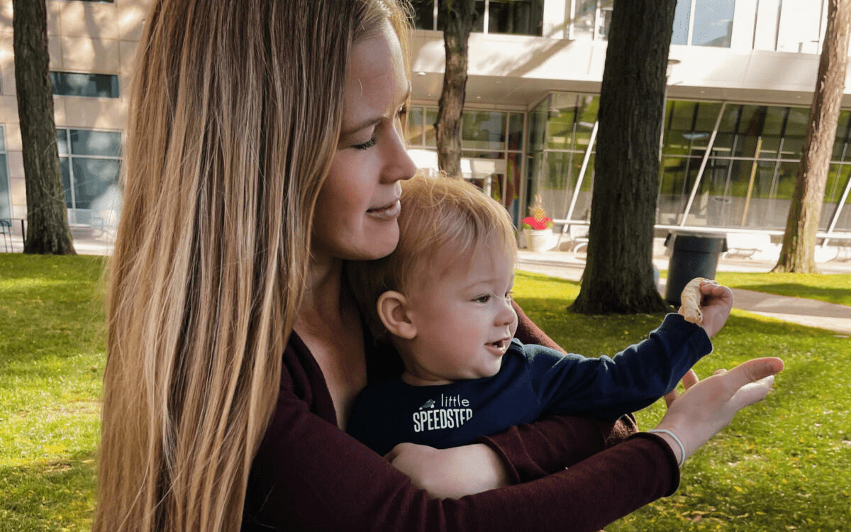 Woman holding a baby on a lawn in front of a building