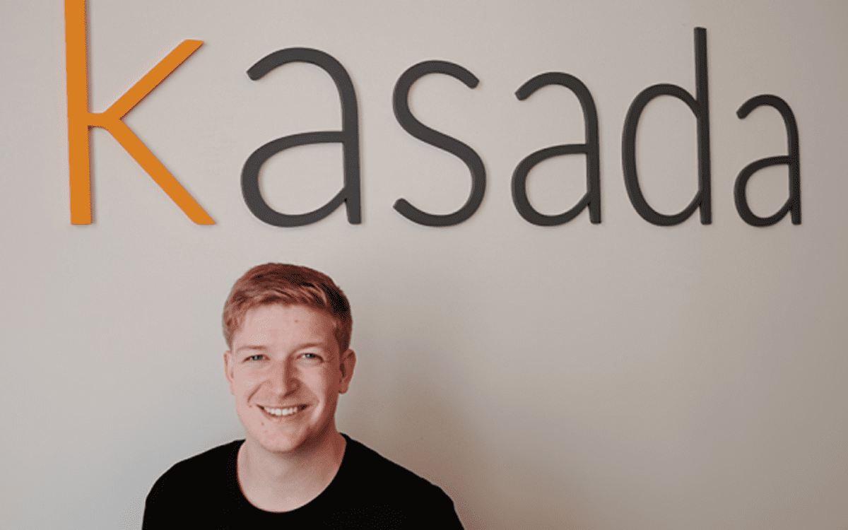 Kasada Founder Sam Crowther standing in front of Kasada logo hung on wall