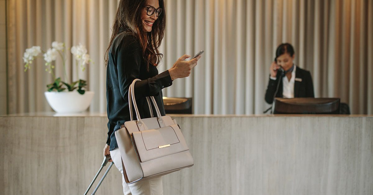 Female business traveler walking in hotel hallway checking in to her room with her mobile phone