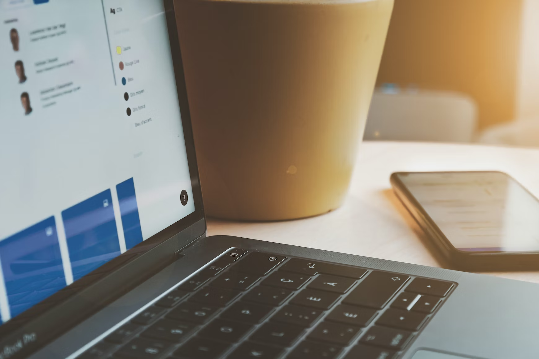 A laptop is on a table next to a phone and a cup of coffee.