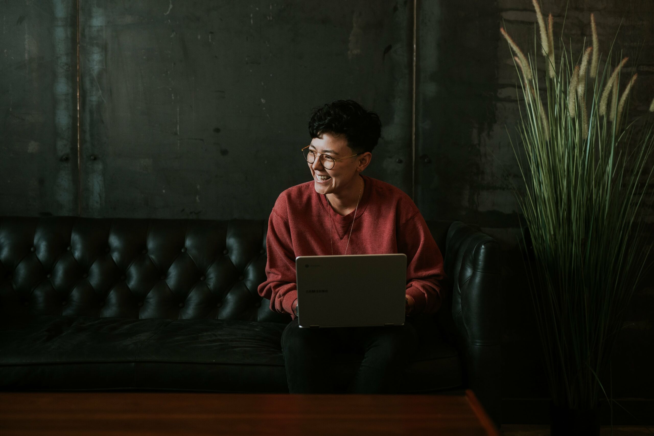A woman sitting on a couch using a laptop for bot management purposes.