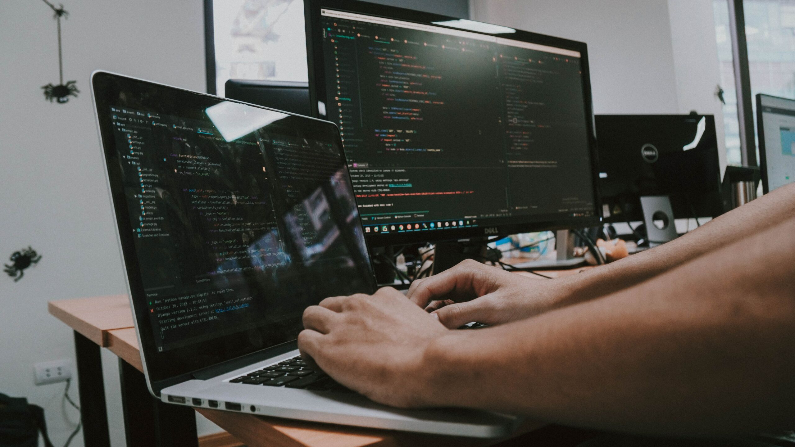 A man is working on a laptop in front of a computer screen.