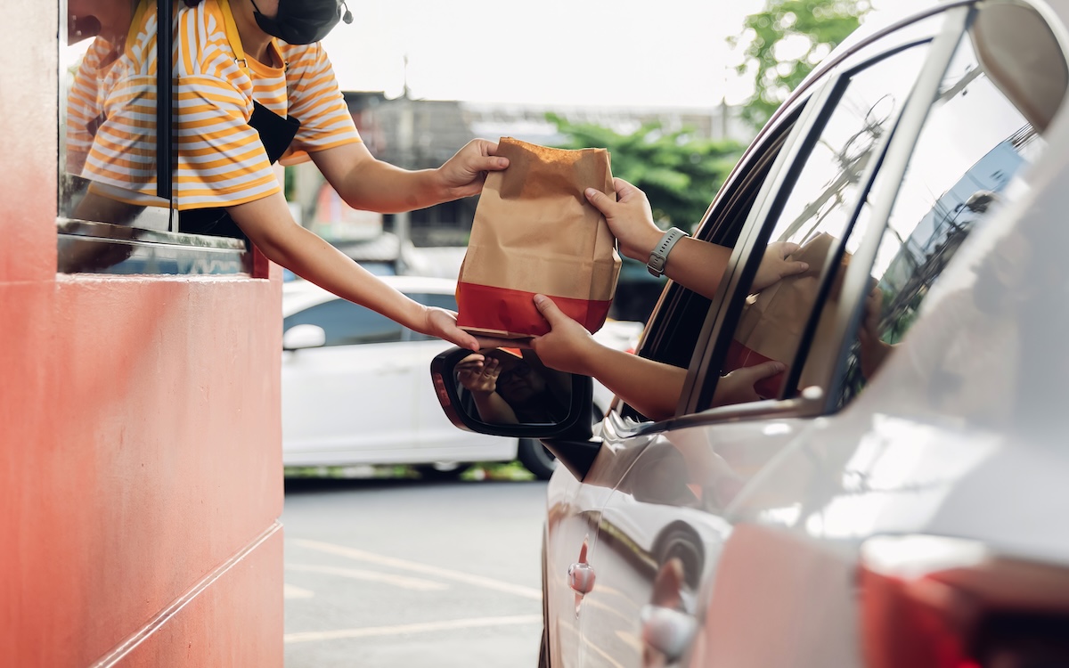 Hand Man in car receiving coffee in drive thru fast food restaurant. Staff serving takeaway order for driver in delivery window. Drive through and takeaway for buy fast food for protect covid19.